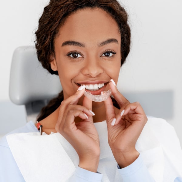 Transform Your Smile with Invisalign at Bawa Dentistry A woman is holding her Invisalign and smiling