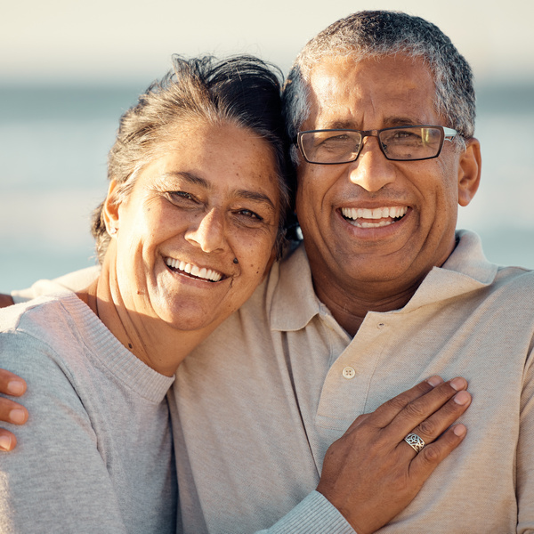 Closeup portrait of an senior affectionate mixed race couple standing on the beach and smiling during sunset outdoors. Hispanic couple showing love and affection on a romantic date at the beach