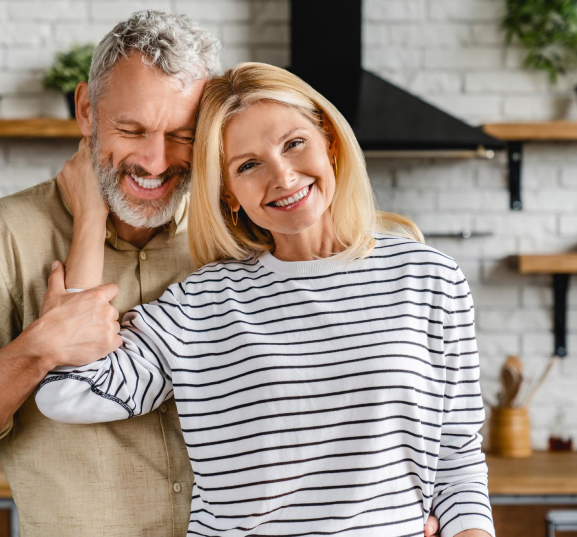 The elderly couple is delighting in each others company, sharing smiles in the kitchen